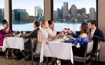 Dining guests enjoying a meal with Boston skyline view on Premier Dinner Cruise on Odyssey.