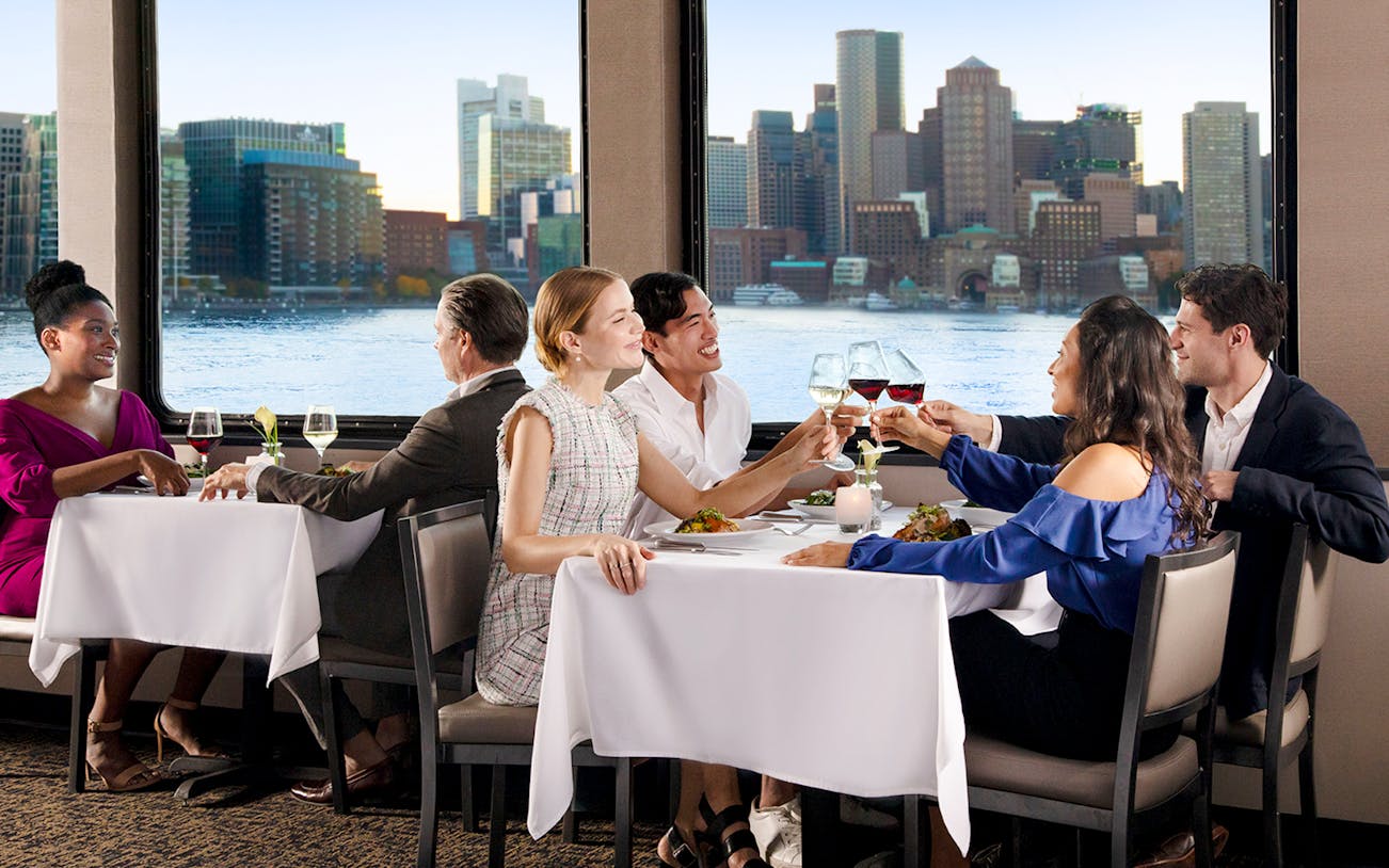 Dining guests enjoying a meal with Boston skyline view on Premier Dinner Cruise on Odyssey.
