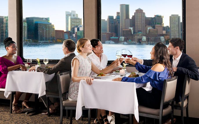Dining guests enjoying a meal with Boston skyline view on Premier Dinner Cruise on Odyssey.