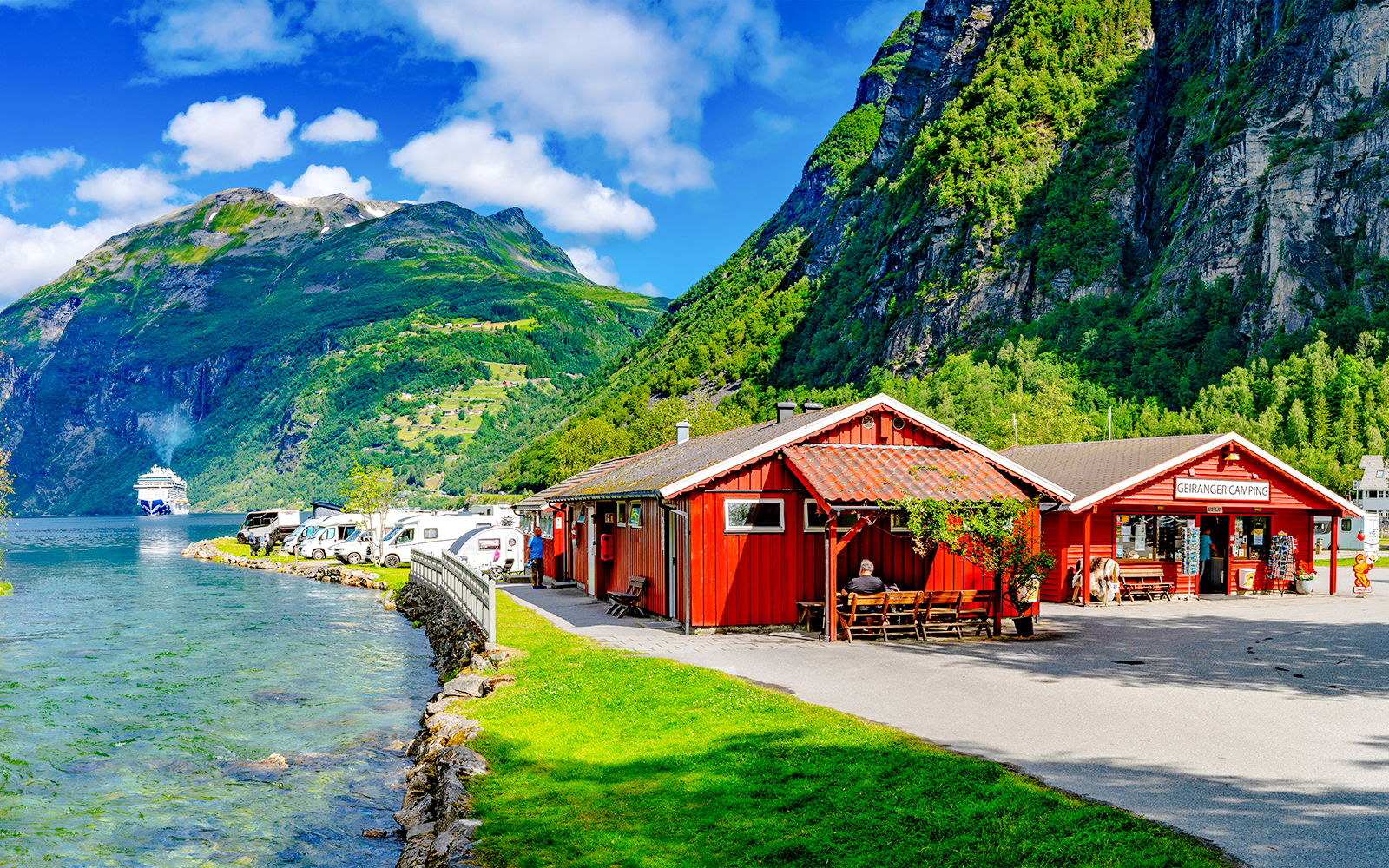 Geirangerfjord Norway with cruise ship, red cabins, and camper vans along the water.