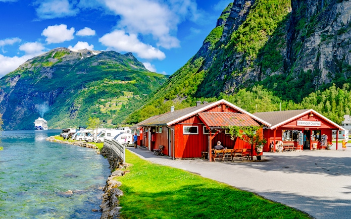 Geirangerfjord Norway with cruise ship, red cabins, and camper vans along the water.