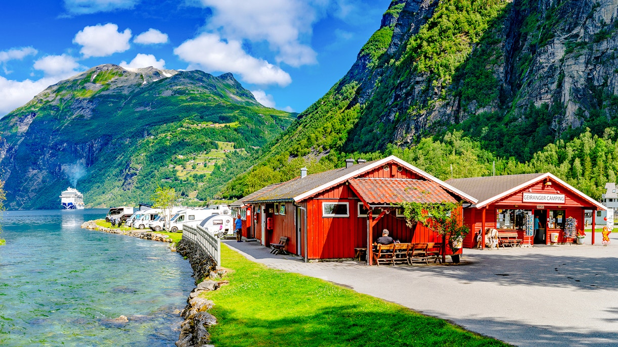 Geirangerfjord Norway with cruise ship, red cabins, and camper vans along the water.
