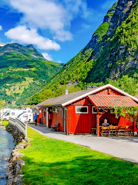 Geirangerfjord Norway with cruise ship, red cabins, and camper vans along the water.