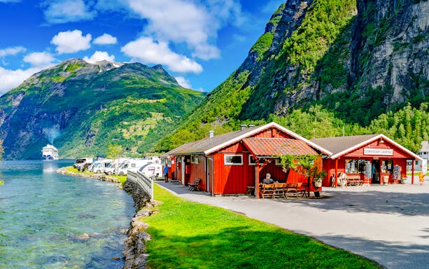 Geirangerfjord Norway with cruise ship, red cabins, and camper vans along the water.