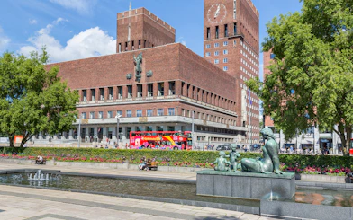 Oslo City Hall with a red hop-on hop-off bus in front, part of the Oslo sightseeing tour.