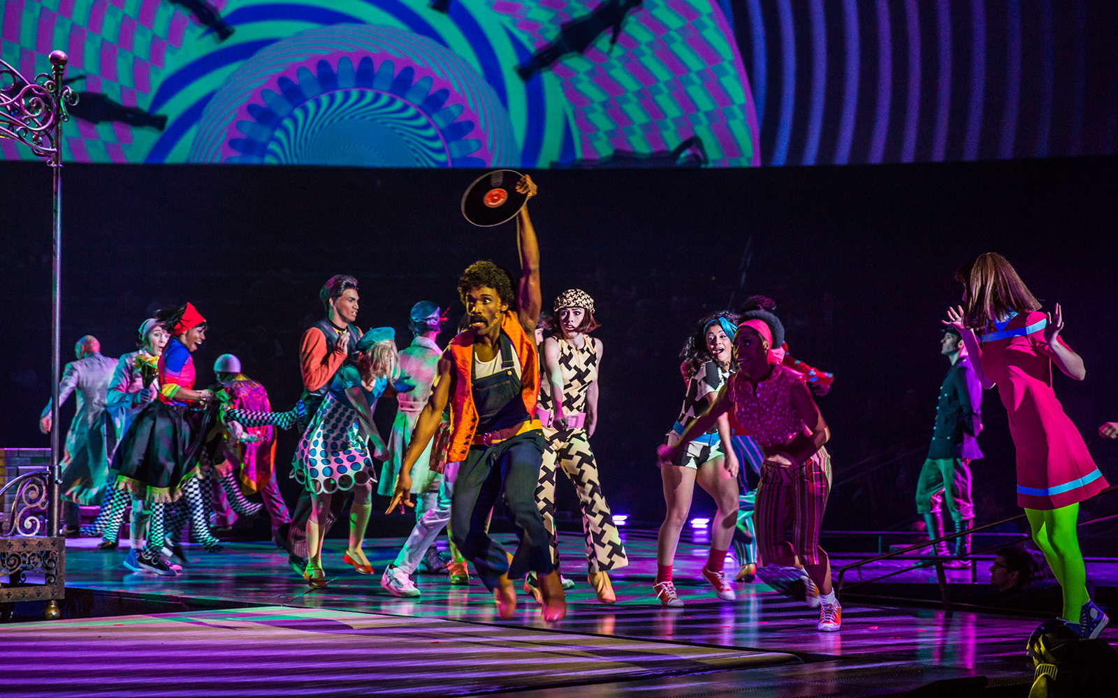 Performers dancing energetically in The Beatles LOVE show with vibrant costumes and psychedelic backdrop.