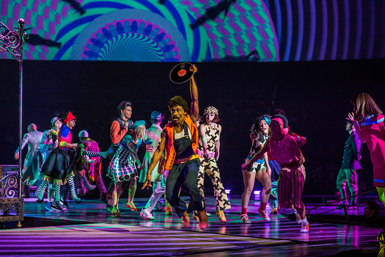 Performers dancing energetically in The Beatles LOVE show with vibrant costumes and psychedelic backdrop.