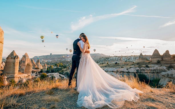 Couple embracing with hot air balloons over Cappadocia's unique rock formations.