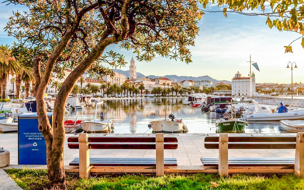 Boats docked along the Riva promenade in Split, Croatia with cityscape and mountains in the background.