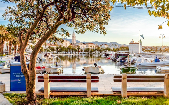 Boats docked along the Riva promenade in Split, Croatia with cityscape and mountains in the background.