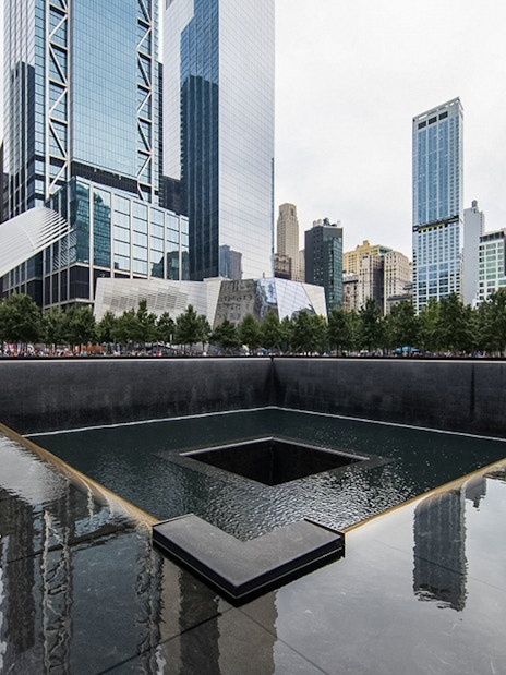 9/11 Memorial waterfall with city skyline in the evening, New York City.