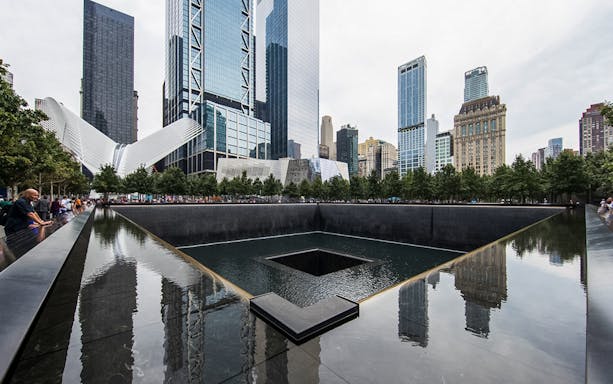 9/11 Memorial waterfall with city skyline in the evening, New York City.