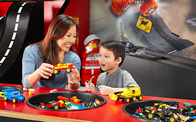Child and adult building LEGO cars at indoor playground, LEGOLAND Discovery Centre Berlin.