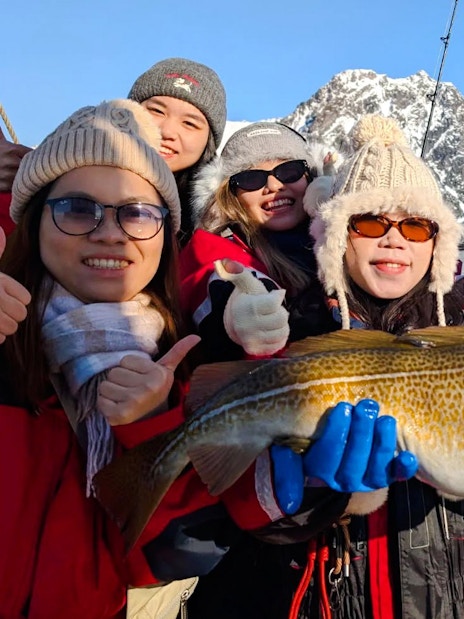 Group holding Atlantic cod on fishing boat cruise, Lofoten, with snowy mountains in background.
