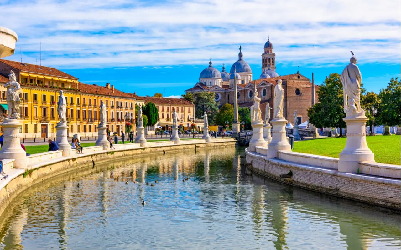 Prato della Valle canal and statues in Padua, Italy, with historic buildings in the background.