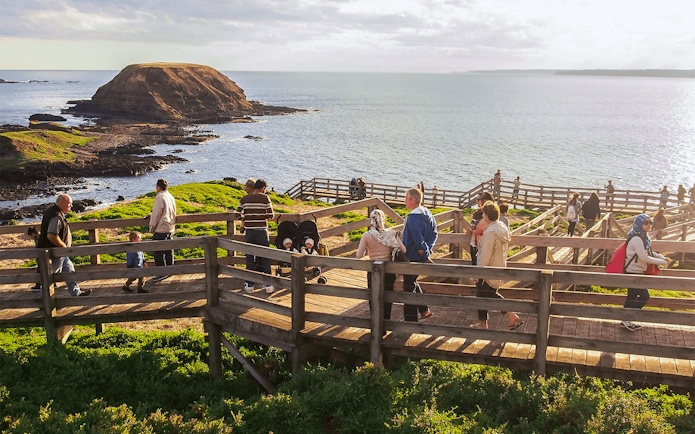Visitors walking along Nobbies Lookout boardwalk with ocean view, Phillip Island, Australia.