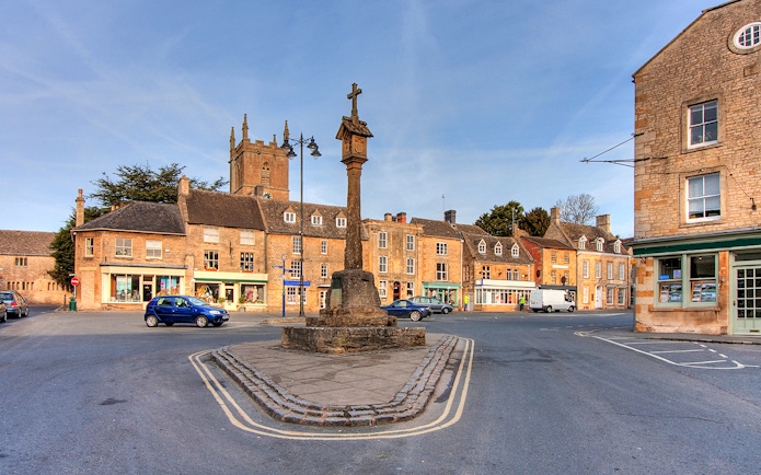 Cotswolds village square with historic stone buildings and market cross.