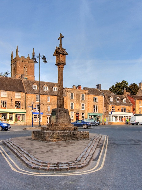 Cotswolds village square with historic stone buildings and market cross.