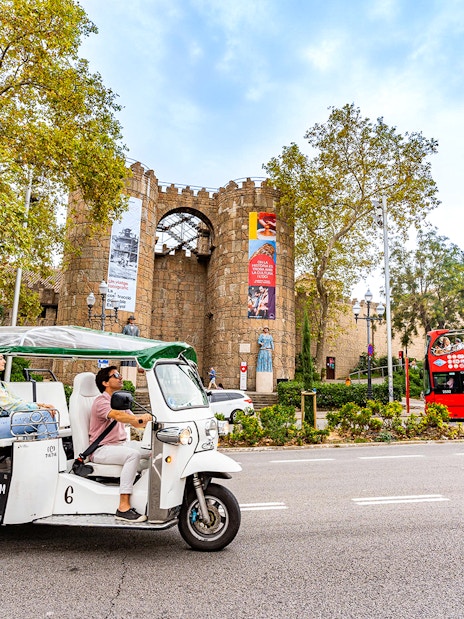 Tuk tuk tour passing by Poble Espanyol entrance in Barcelona.