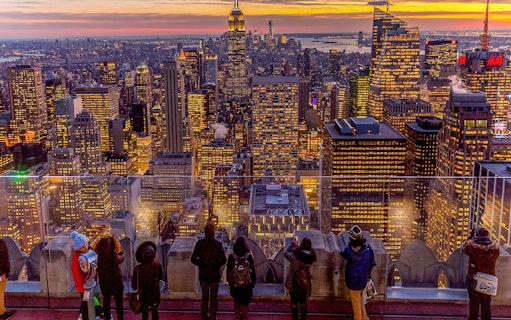 Visitors viewing Manhattan skyline at sunset from Top of the Rock, Rockefeller Center, New York.