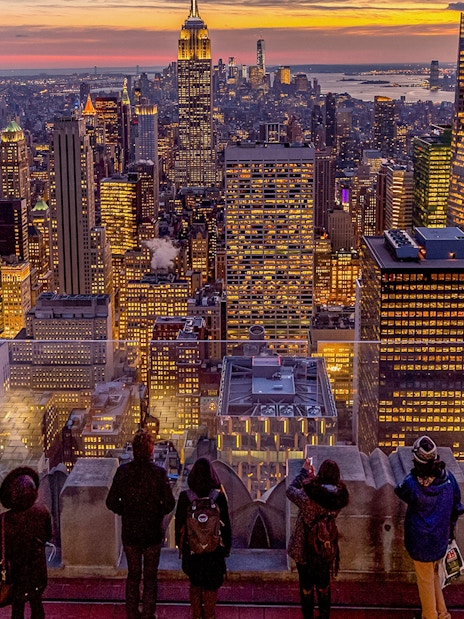 Visitors viewing Manhattan skyline at sunset from Top of the Rock, Rockefeller Center, New York.