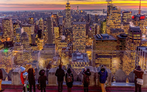 Visitors viewing Manhattan skyline at sunset from Top of the Rock, Rockefeller Center, New York.