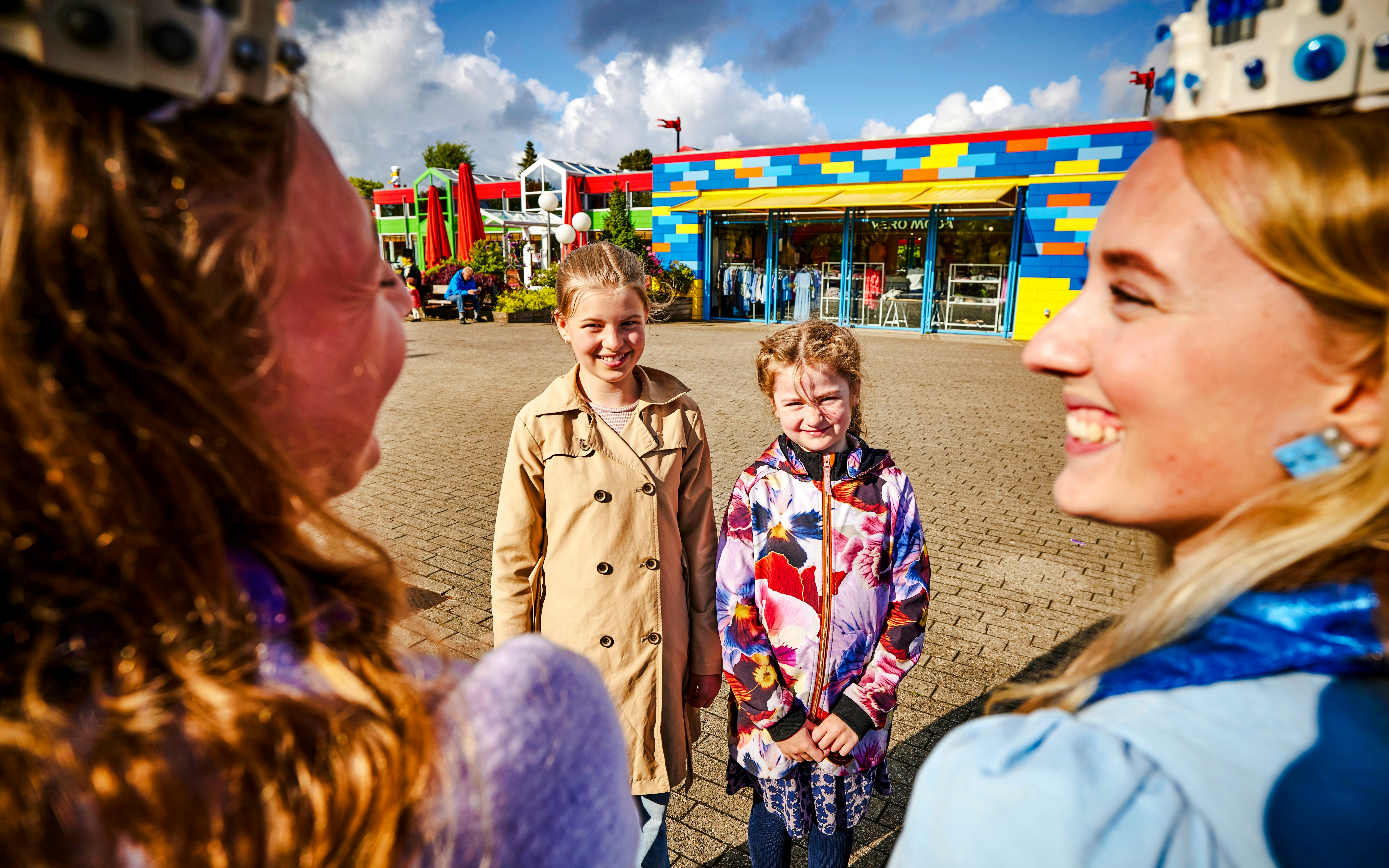 Kids enjoying a sunny day at LEGOLAND Billund with colorful buildings in the background.