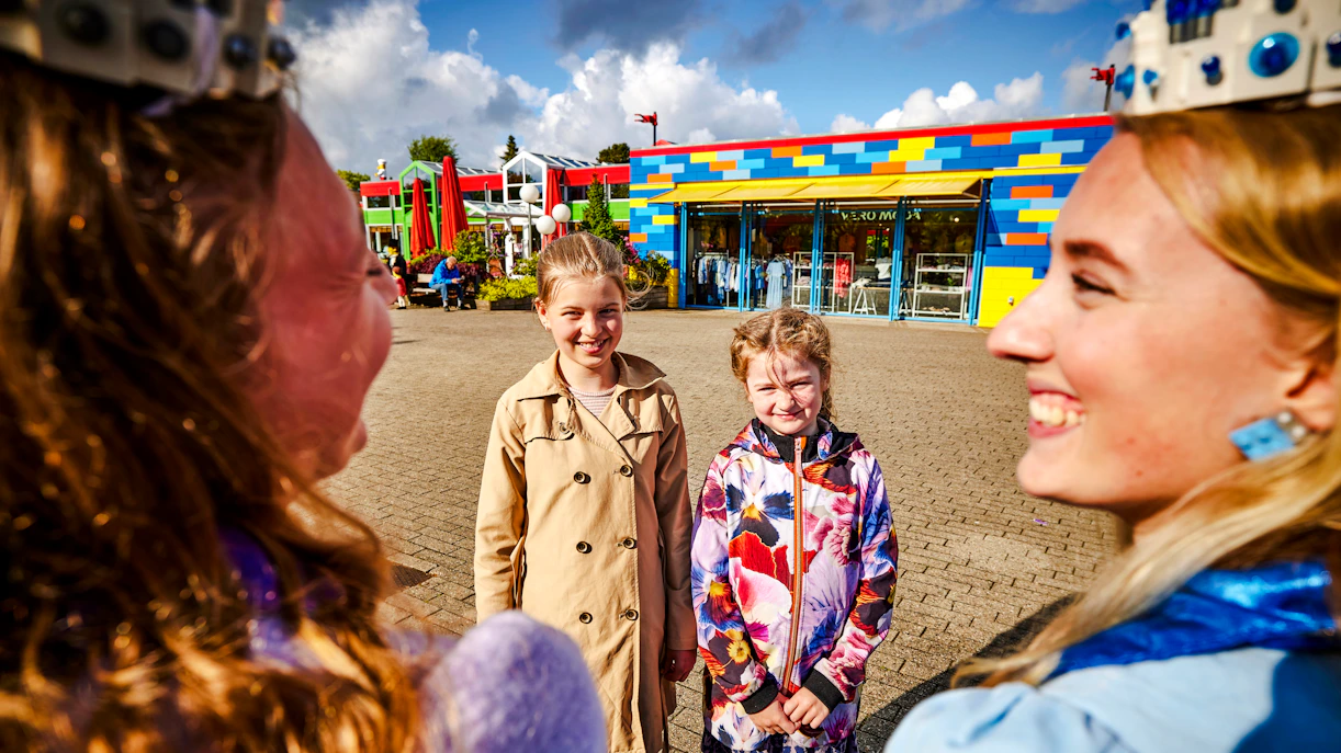 Kids enjoying a sunny day at LEGOLAND Billund with colorful buildings in the background.