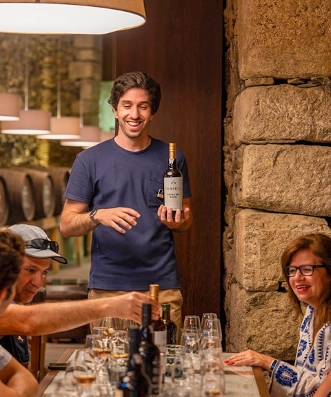 Tourists with guide tasting wine in Douro wine cellar.