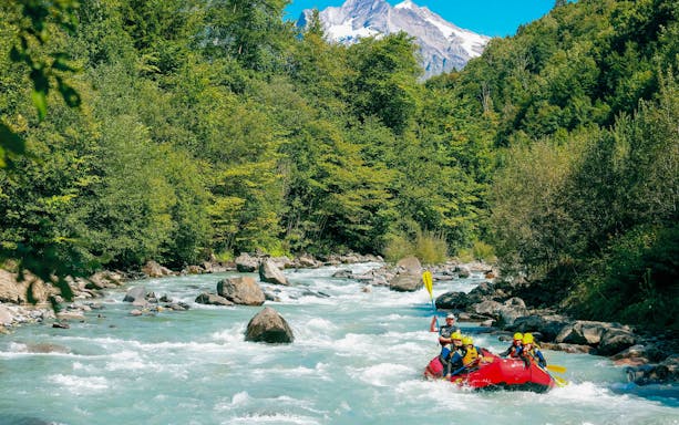 River rafting adventure on a turquoise river in Interlaken with lush green forest and mountains.