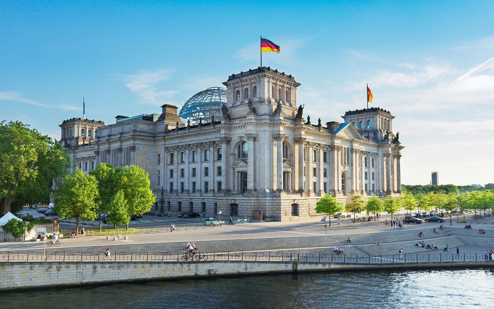Reichstag building in Berlin's Government District with people and river in foreground.