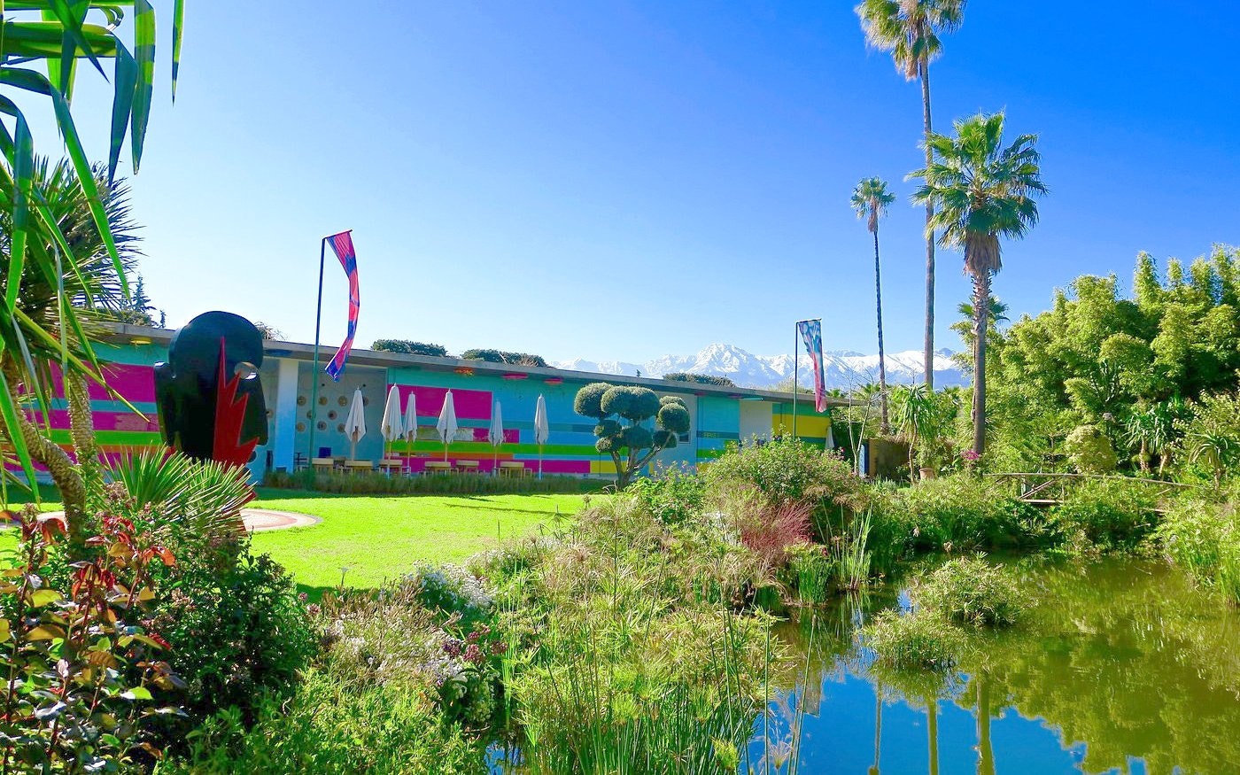 Colorful building and lush garden with pond at ANIMA Garden, Morocco.