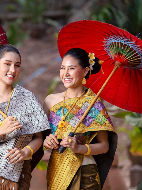 Two women in traditional Thai attire holding decorative umbrellas.
