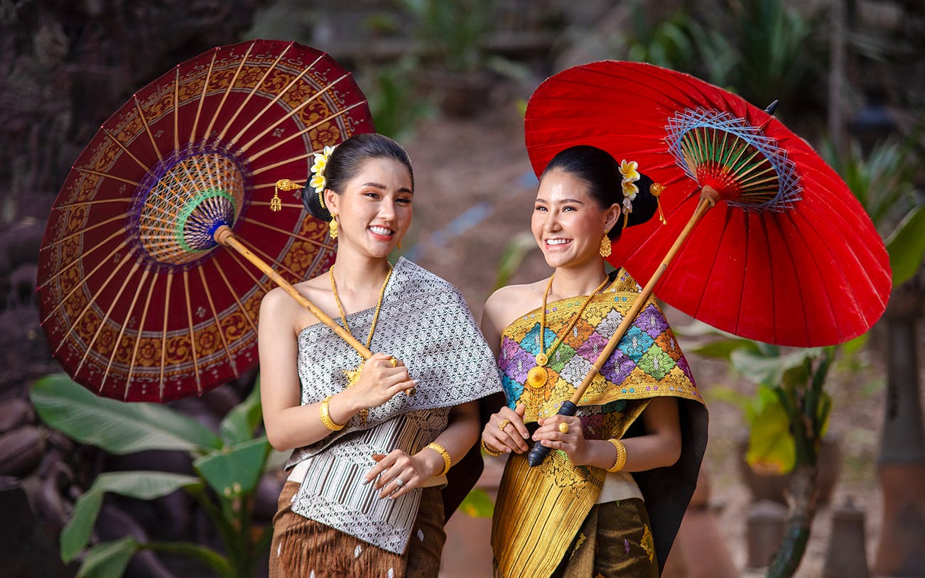 Two women in traditional Thai attire holding decorative umbrellas.