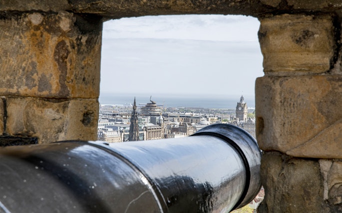 Cannon view from Edinburgh Castle overlooking cityscape and sea.