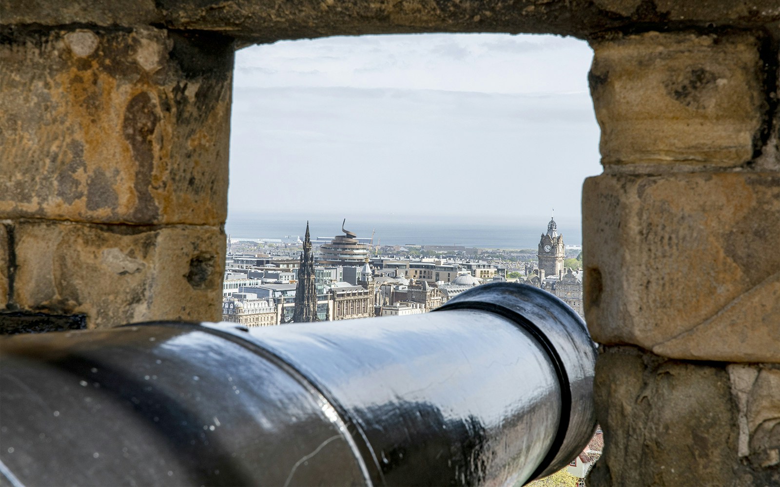 Cannon view from Edinburgh Castle overlooking cityscape and sea.