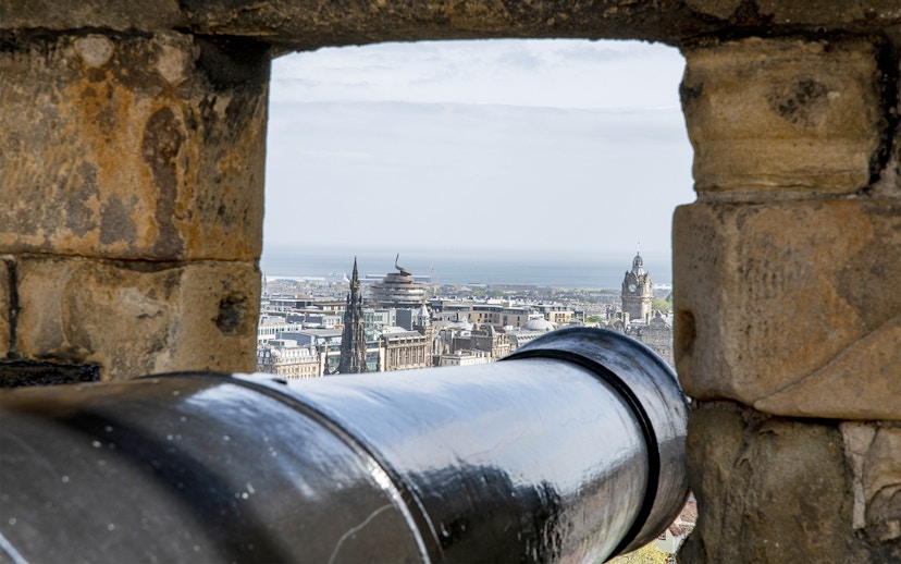 Cannon view from Edinburgh Castle overlooking cityscape and sea.