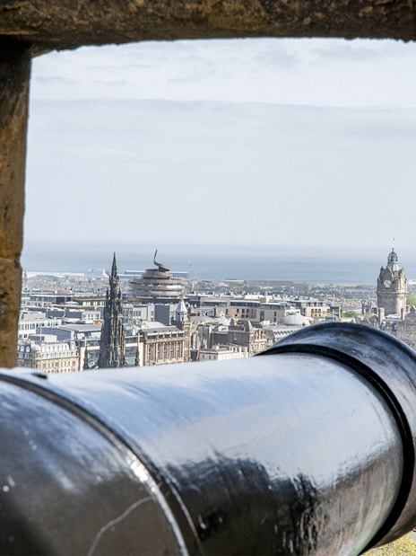Cannon view from Edinburgh Castle overlooking cityscape and sea.