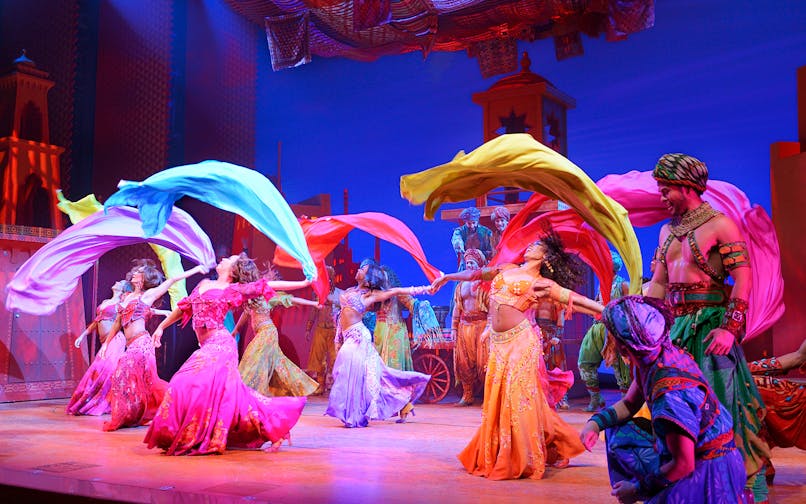 Performers in colorful costumes dancing with flowing scarves in an Aladdin stage show.