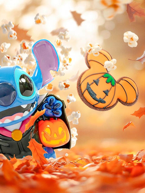 Stitch in Halloween costume with pumpkin bucket, surrounded by autumn leaves at Disneyland Paris.
