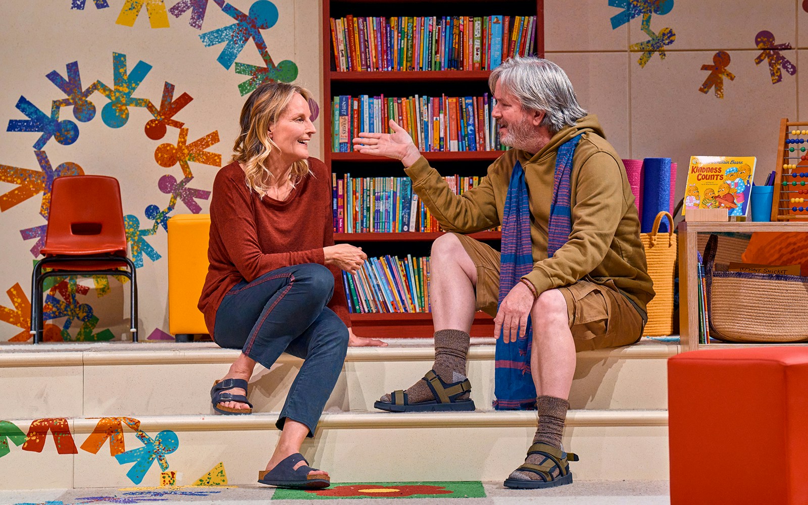 Two people sitting on steps in a colorful library setting, discussing Eureka Day.