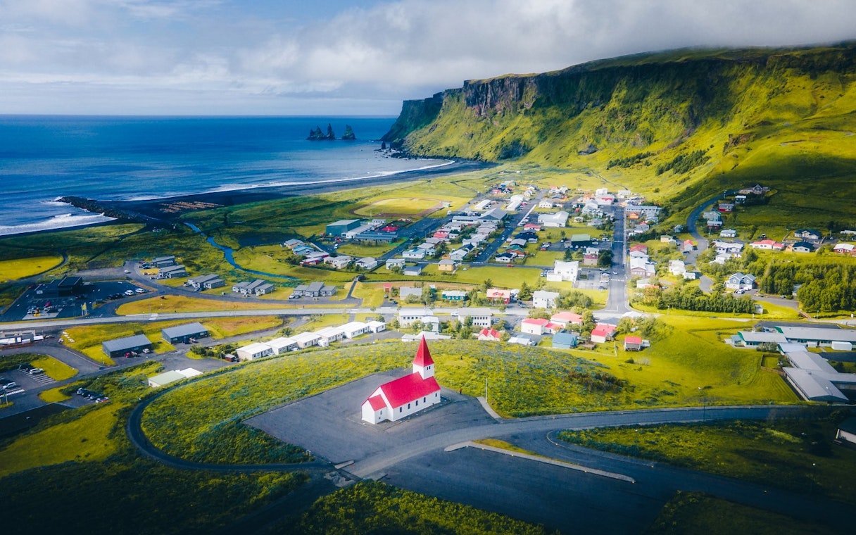 Aerial view of Vik, Iceland, featuring a red-roofed church and coastal landscape.
