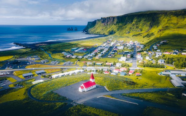 Aerial view of Vik, Iceland, featuring a red-roofed church and coastal landscape.