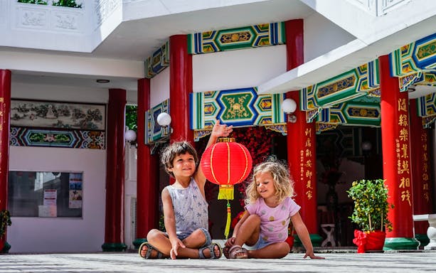 Children with a red lantern at a colorful temple entrance, Batu Caves tour.