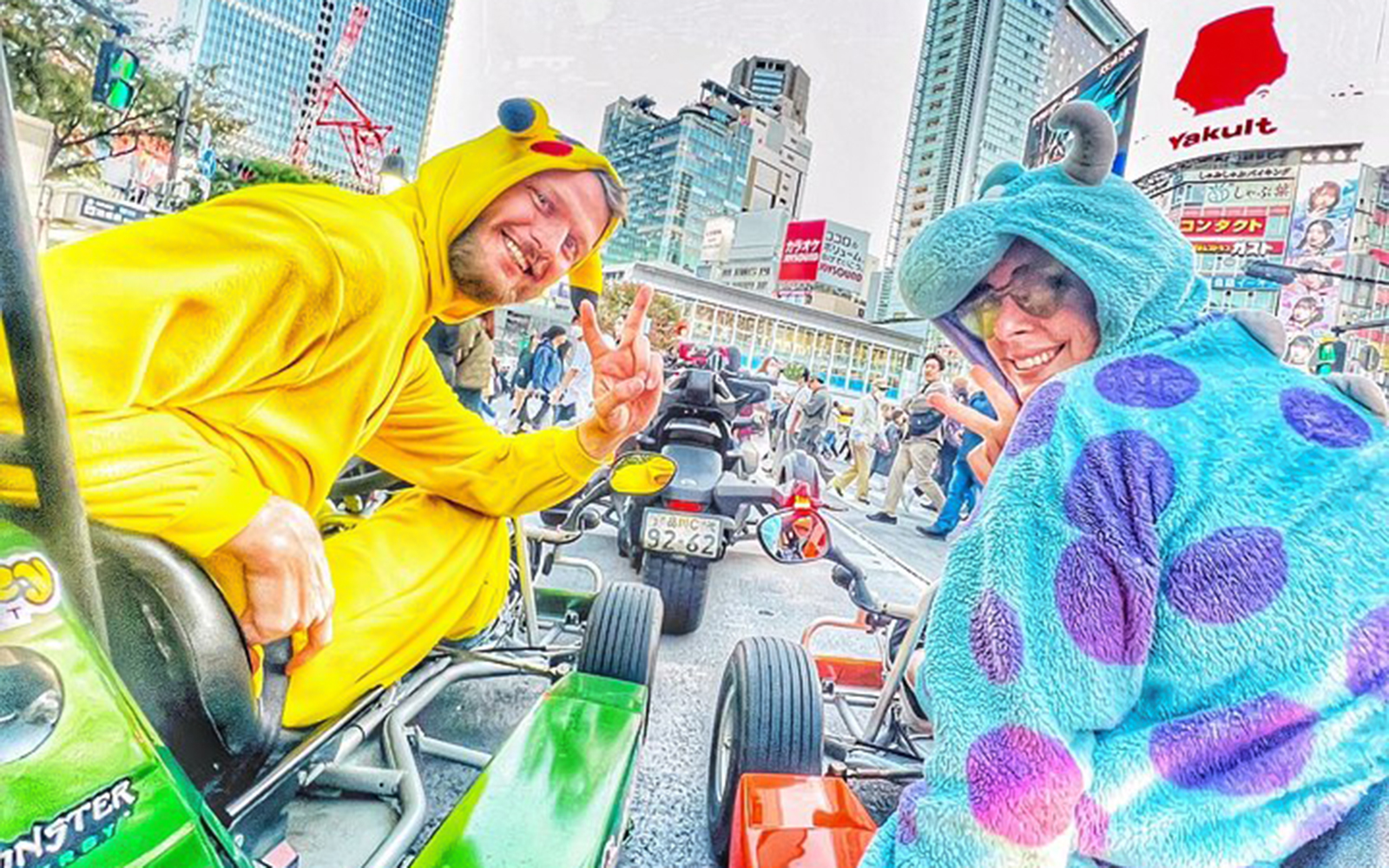 Man in Pikachu costume and woman in Sulley costume in go-karts, Shibuya crossing.
