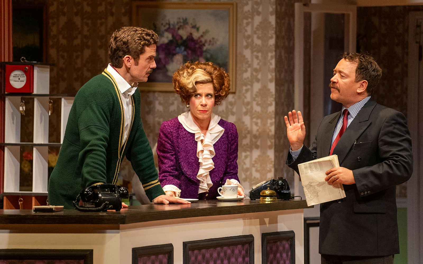 Hotel reception scene with three actors in a Fawlty Towers play.