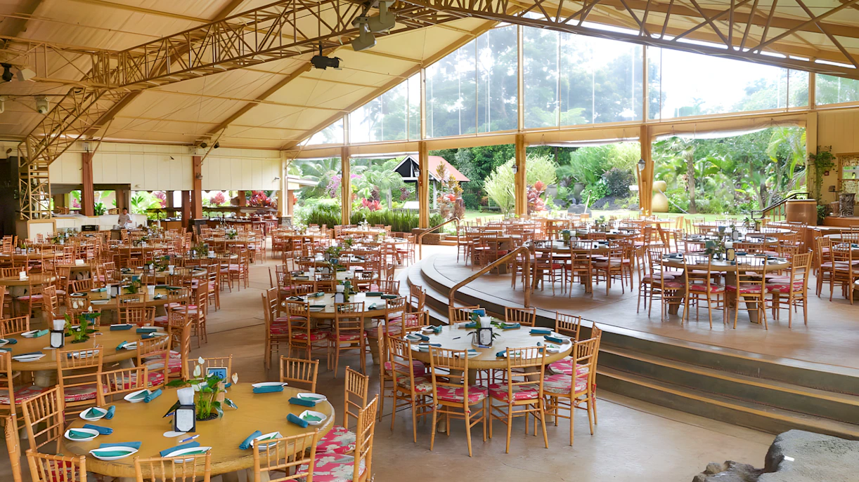 Open-air dining area set for a Hawaiian buffet luau feast with tropical garden views.