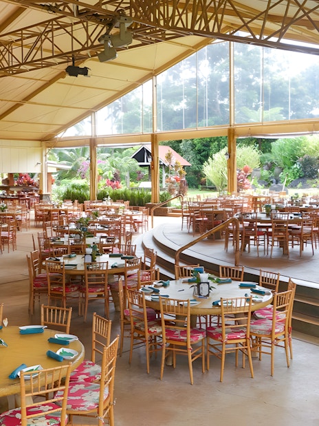 Open-air dining area set for a Hawaiian buffet luau feast with tropical garden views.