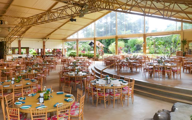 Open-air dining area set for a Hawaiian buffet luau feast with tropical garden views.