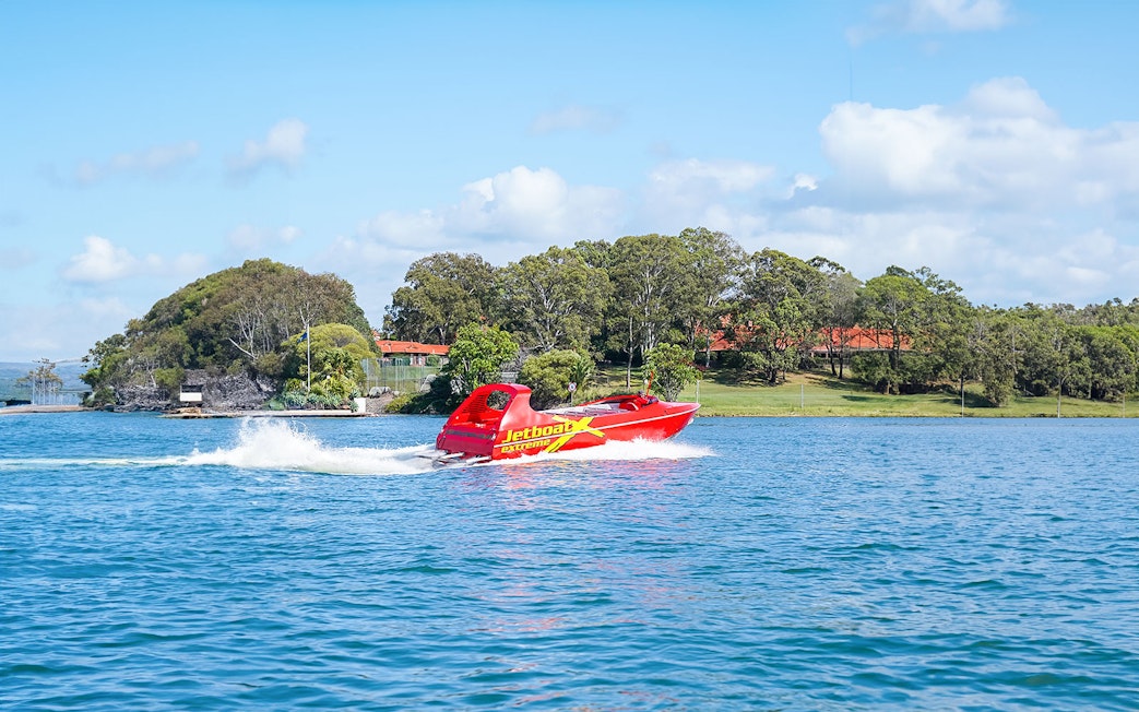 Red jet boat speeding on a blue river with green trees in the background.